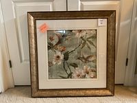 Front view of the framed artwork showing the full piece including the gold-tone frame, white mat border, and the print featuring birds and flowers.