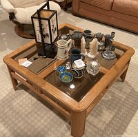 Wide view of all items on a square wooden coffee table with glass inlays, showing the full collection including two onyx horse head bookends, multiple pewter items, ceramic mugs and jars, glass candle holders, and a table lamp with bamboo artwork.