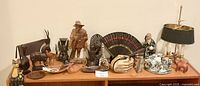 Full view of various decorative art deco pieces arranged on a wooden table including figurines, a fan, ceramic items, and a lamp