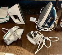 Front view of four irons arranged on wooden floor with cords