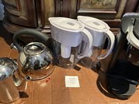 Photo of the Keurig coffee maker, Brita water pitchers, stainless steel kettles, and stainless steel teapot on a wooden floor.