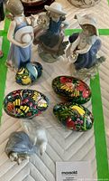 Photo showing three Lladro porcelain figurines of girls, four vividly hand-painted decorative eggs, and one ceramic duck figure with ducklings on display.