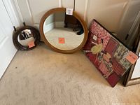 View of two round mirrors and framed Henri Matisse print leaning against wall on carpeted floor.