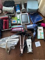 Wide shot showing the full lot with hair tools, wallets, e-reader, and other personal care items arranged on hardwood floor.