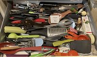 Top view of drawer with assorted kitchen utensils including graters, peelers, spoons, and spatulas showing quantity and condition