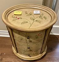 Front view of the oval side table showing its three drawers decorated with hand-painted leaves and flowers.