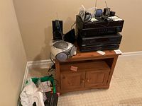 Technics CD carousel changer and Yamaha AV receiver stacked on solid wood stand with boom box on side. Sony headphones and other small items on top. Green plastic bin with miscellaneous items on floor beside stand.