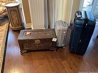Overview of the two Samsonite spinner suitcases and the carved Chinese wood trunk placed next to each other on hardwood floor.