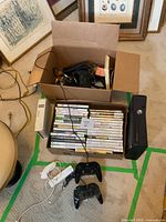 Overhead view of black Xbox 360 S console, white Nintendo Wii console, stacked game cases and controllers