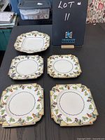 Photo displaying all five Aynsley antique plates on dark table, showing grapevine and leaf pattern around edges and scalloped shape.