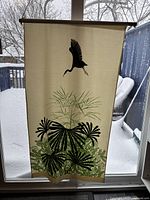Cloth hanging banner displayed in front of a window showing a black bird silhouette and green leaves design on cream fabric.