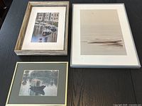Top view of three framed boat prints arranged on a black wooden surface, showing frames and prints.