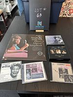 Photo of the entire lot showing one vinyl album and five CD cases arranged on a table with a box labeled 'Lot # 63'.
