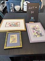 Three framed Marilyn Pike floral prints on a black table with a sign for lot number 34.