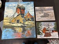 Three canvas artworks displayed on dark surface: large original oil painting of windmills and two smaller landscape prints