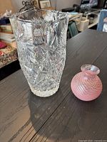 Clear pinwheel crystal vase with detailed cut patterns and pink bud vase together on table, showing overall size and style.
