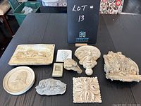 Nine assorted plaster decor pieces arranged on a table showcasing different shapes and designs with visible wear and chips.