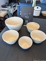 Five creamy white plant pots of varying sizes arranged on a table with a blackboard noting the lot number.