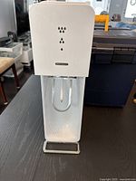 Front view of white SodaStream carbonation machine with clear plastic bottle attached.