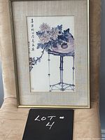 Framed watercolour still life floral print, showing purple flowers on a round table with calligraphic script alongside. Slim gold-tone frame and linen-look matte surround.
