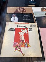 Photo showing a stack of vinyl albums featuring Barbra Streisand's 'Funny Girl' album cover in front, others include 'One Voice' and a collaborative album with Kristofferson.