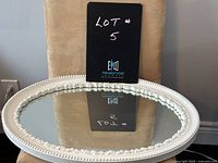 White oval mirror laying flat on a chair showing the floral decorative border around the frame, mirror reflecting a sign reading 'LOT 5'.