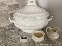 White ceramic Amora Italian soup tureen with lid and side handles shown on countertop with smaller creamer and sugar bowl items in front.