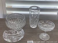 Photo of four vintage clear cut glass crystal pieces arranged on a wooden surface in front of window blinds.