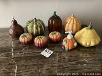 Nine-piece set of decorative ceramic pumpkins and one soap dispenser, arranged on a marble surface.