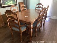 Photo of full rectangular Ethan Allen dining table with eight ladderback chairs and extensions in a bright room with wooden floor.