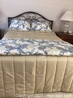Full view of bed with beige coverlet and blue and beige paisley floral bedspread and pillow shams arranged on a metal bed frame.