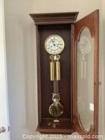 Full view of the Ethan Allen wall clock inside a wooden case with glass door open showing brass weights and pendulum.