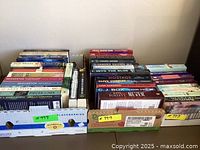 Two cardboard boxes filled with a variety of fiction books stacked with spines visible, showing authors and titles.