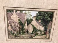 Close-up of the framed decorative picture showing the village scene focusing on the cottages, stone walls, and greenery.