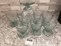 Set of eight green glass footed tumblers displayed in an upright position showing etched decorative patterns.