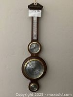 Full view of the polished brass and wood wall clock including the thermometer at top, clock face in middle, and barometer at bottom.