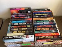 Two stacks of fiction paperback books showing titles primarily by James Patterson plus books by Michael Connelly and John Grisham.