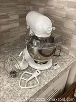 White KitchenAid Ultra Power stand mixer with the stainless steel bowl and three mixer attachments (wire whisk, flat beater, dough hook) arranged on a countertop.