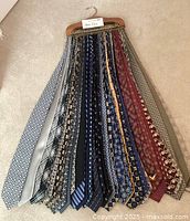 Photo of men's dress ties in various designs and colors hung on a wooden tie hanger.