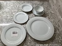 Full place setting pieces including various plates, bowl and cup with embossed white floral design and platinum trim on white porcelain.