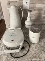 Four small kitchen appliances on a counter: Oster waffle maker, Pampered Chef coffee carafe, Krups coffee grinder, and a manual food chopper