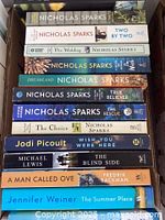 Photo of multiple Nicholas Sparks books stacked in a box, showing titles and authors clearly.