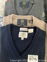 Three sweaters stacked showing gray, beige and navy front panels and V-neck labels