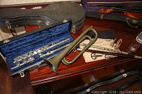 Bugle, flute case open showing silver flute, and instruction book on wooden surface