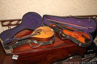 Overview of mandolin and violin in open black hard cases with purple plush lining on wooden cabinet