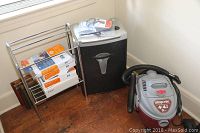 Photo showing the Staples SPL XC200D paper shredder, a 4-gallon Shop-Vac model E87S450 wet/dry vacuum, office paper reams, and chrome metal rack on hardwood floor