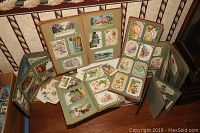 Four albums open on table showing pages with mounted postcards and loose cards scattered