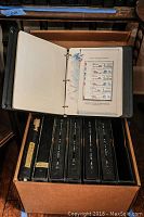 Seven black 3-ring binders in cardboard box with one open to a bicentennial plate block page