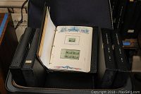 Pullman suitcase open with five black binders inside, one binder open showing stamp album pages