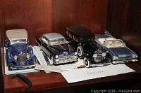 Four Franklin Mint Cadillac model cars displayed on shelf with certificates and paperwork beneath.